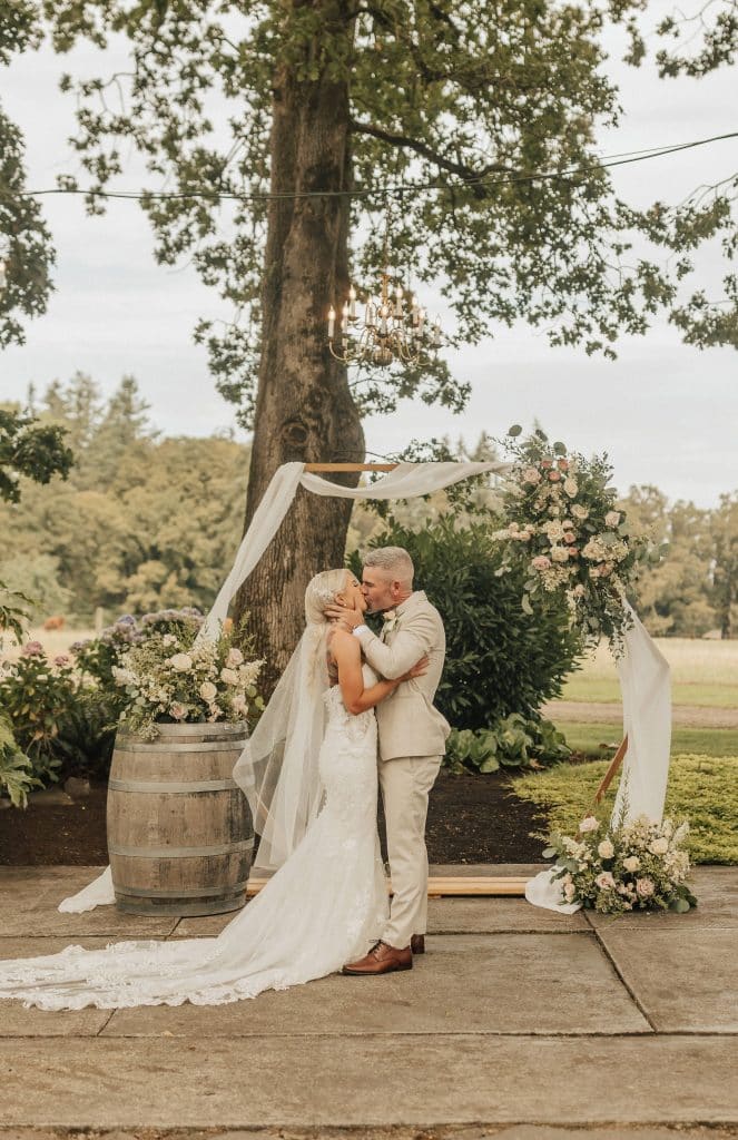 Bride and groom with rustic romantic wedding florals on a hexagon arch and a wine barrel at Postlewaits venue in Oregon